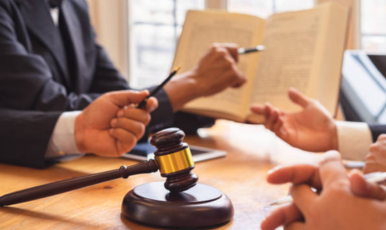 Two people holding a judge's gavel at a table. Expertly grasped for justice